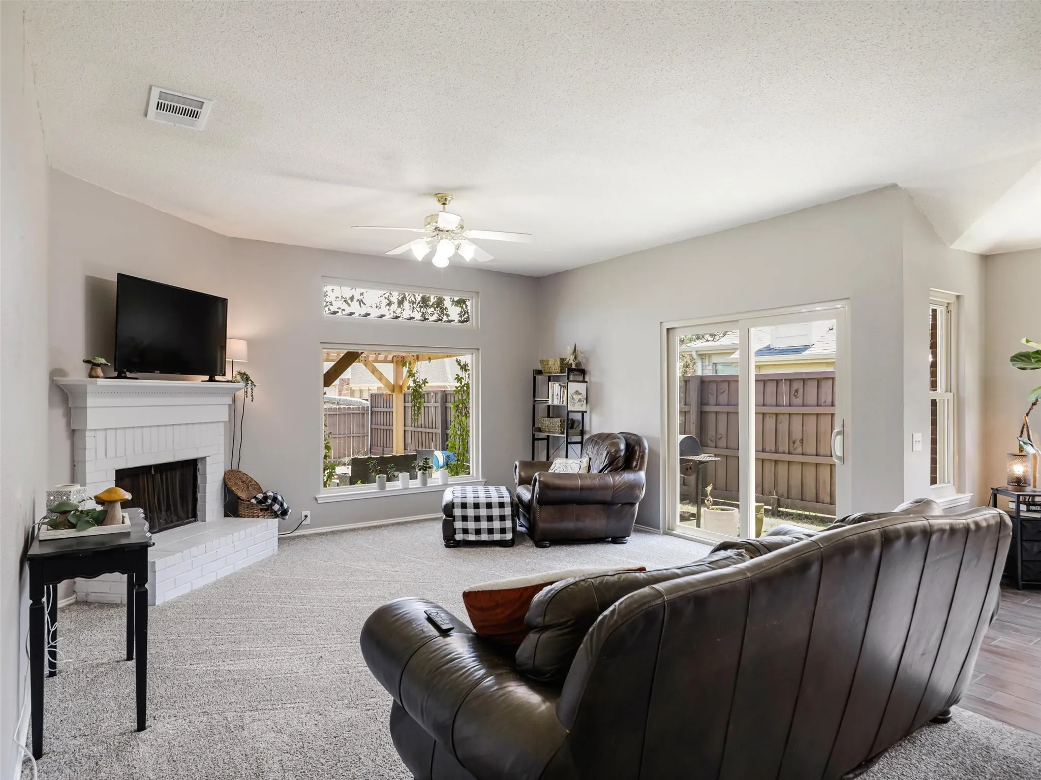 Living area with a white brick fireplace, ceiling fan, and large windows