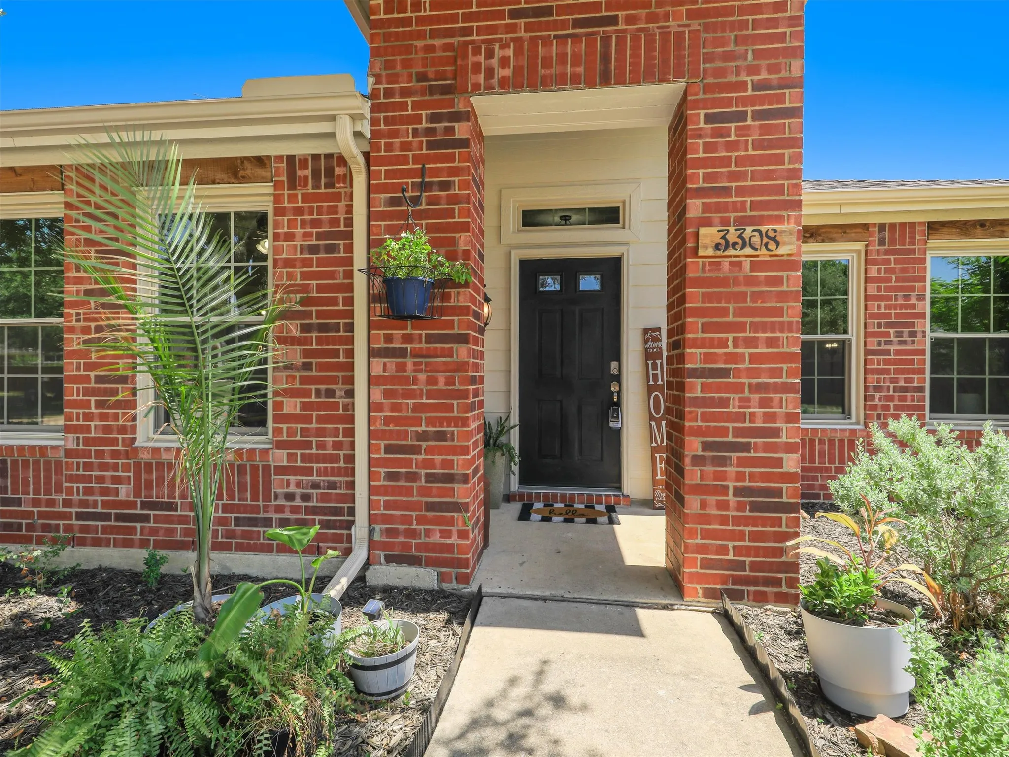 Brick exterior, covered entry, black paneled door, multiple windows, concrete walkway