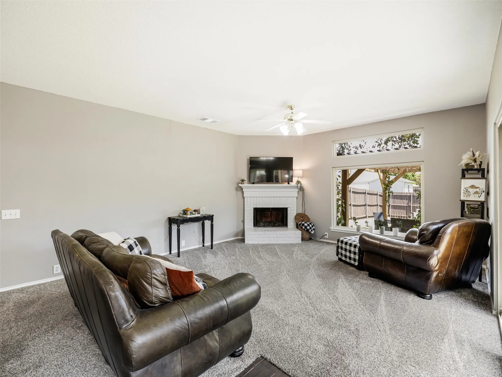 Vaulted ceiling with a ceiling fan, white brick fireplace with a mantel, large window, and carpeted flooring