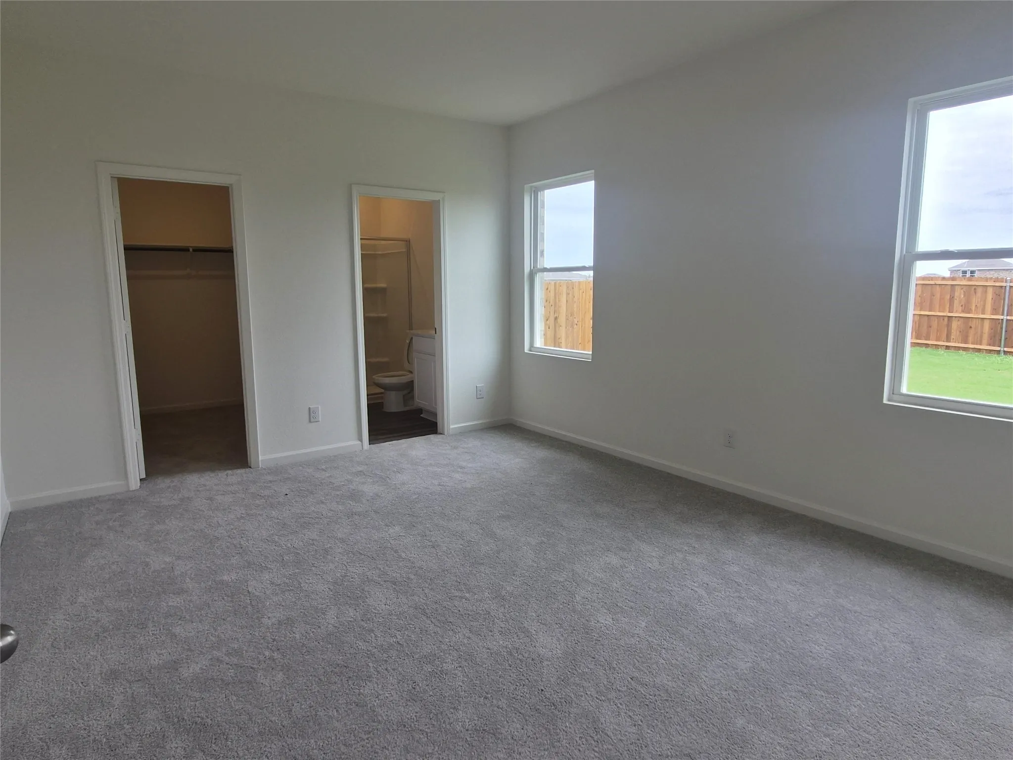 Spacious room with plush gray carpeting, white walls, two double-hung windows, and a walk-in closet