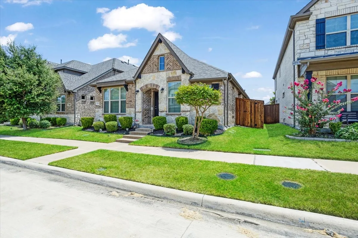 Stone and brick exterior with a gray shingle roof, featuring a landscaped front yard with a walkway and mature trees
