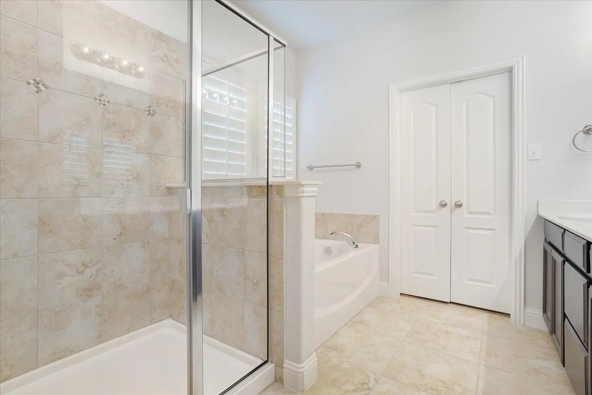 Spacious bathroom featuring a glass-enclosed shower, built-in bathtub, and dual-sink vanity with dark cabinetry