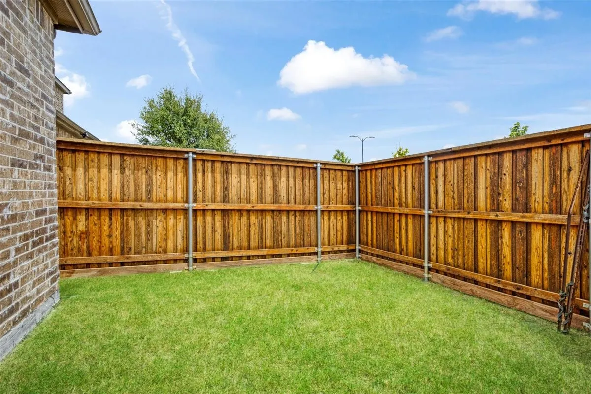 Brick exterior with a wooden privacy fence, metal fence posts, and a grass lawn