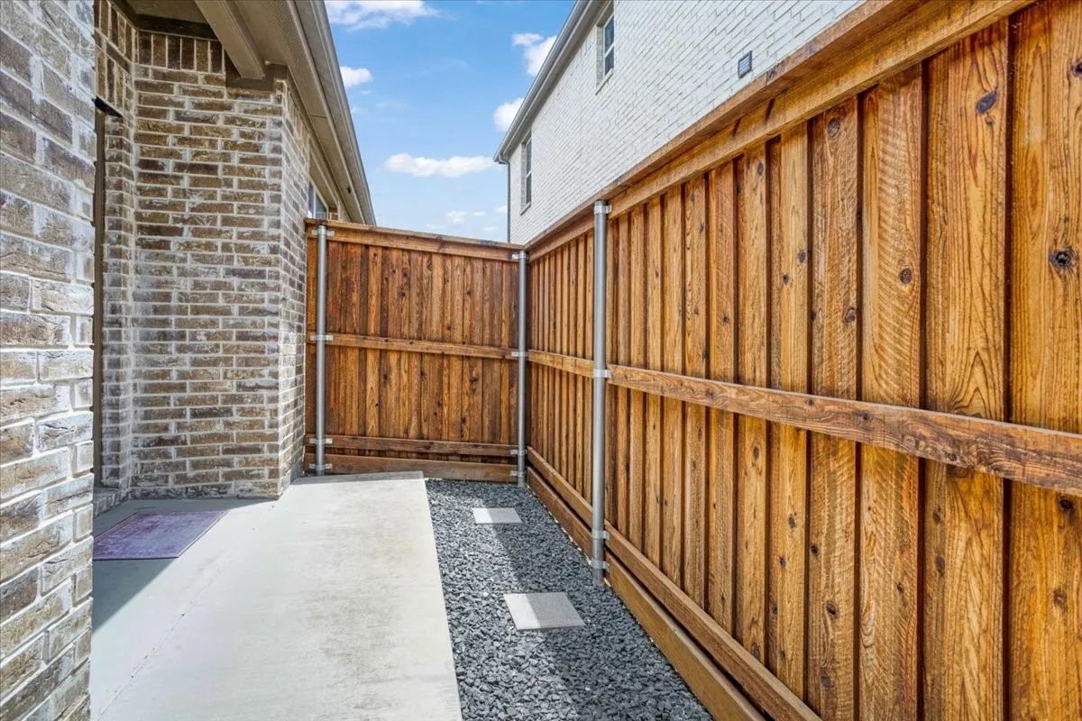 Brick exterior wall with a concrete walkway, complemented by a wood privacy fence and gravel landscaping