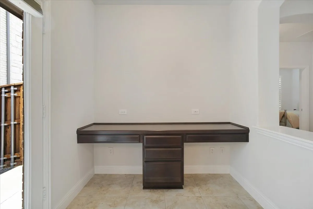 Built-in desk with dark wood-finish cabinetry, neutral tile flooring, and crisp white walls