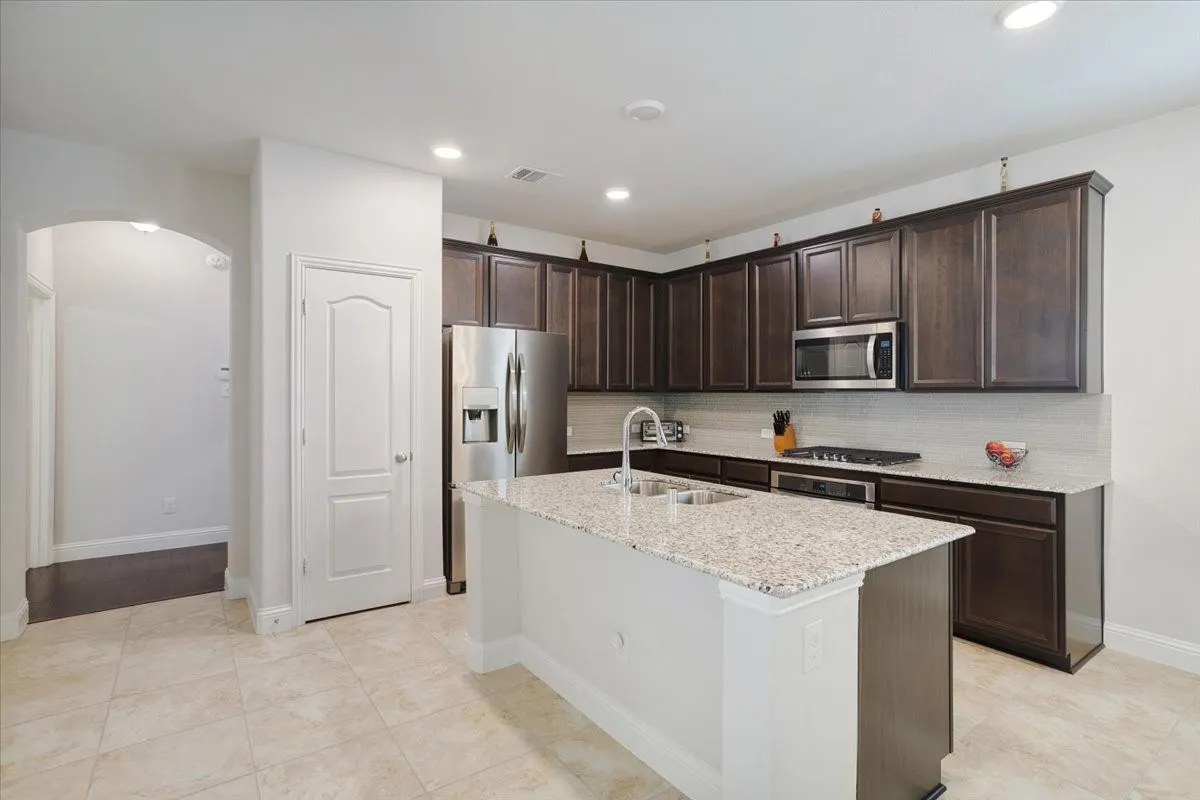 Modern kitchen featuring dark wood cabinetry, a white quartz island with waterfall edge, stainless steel appliances including a built-in microwave, and speckled granite countertops