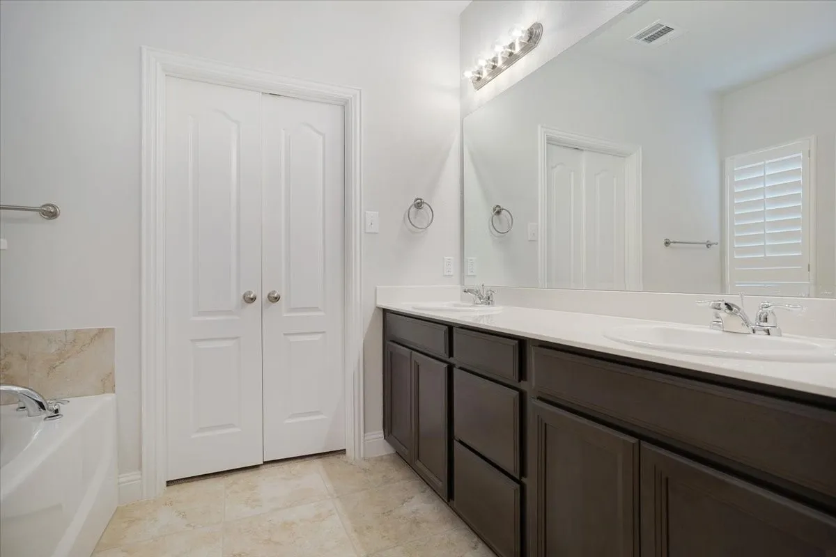 Dual vanity with dark wood-finish cabinetry, white countertops, and chrome fixtures