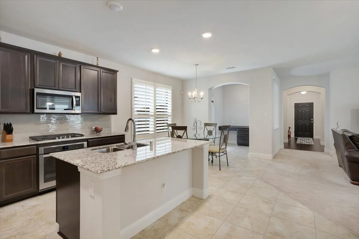 Kitchen island with granite countertop and undermount sink, dark wood-finish cabinetry, stainless steel appliances, and tile flooring