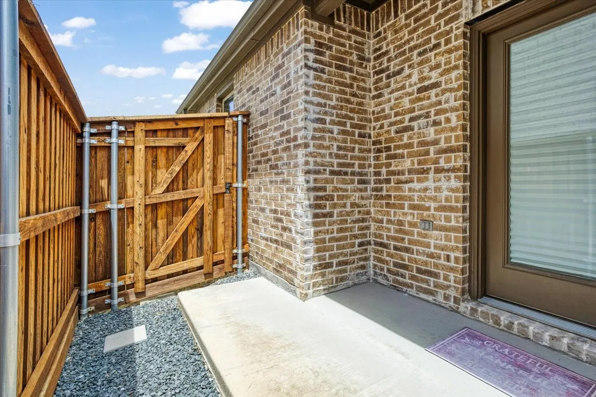Brick exterior wall with a concrete walkway, complemented by a wood privacy fence and gravel landscaping.