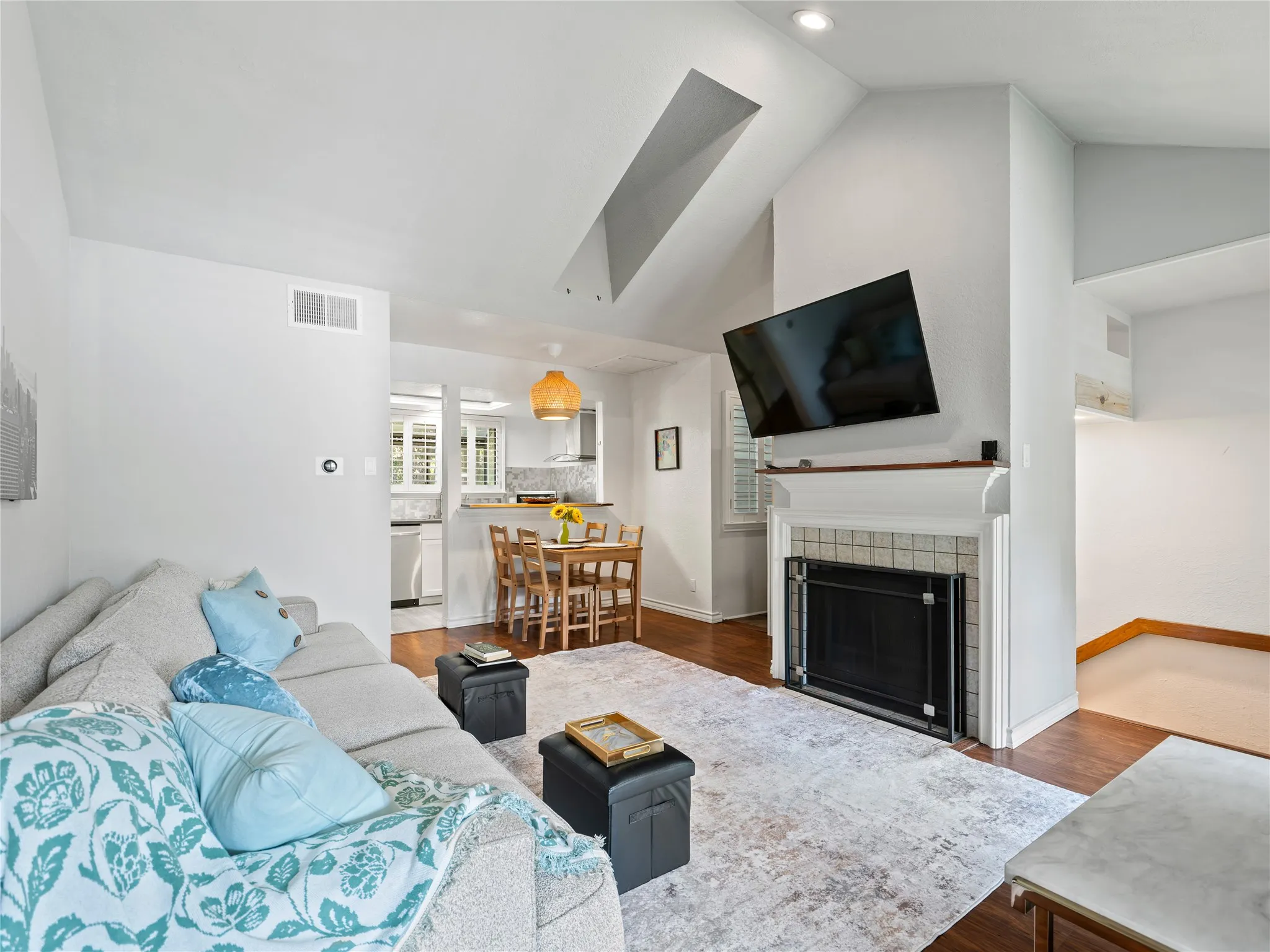 Vaulted ceiling, recessed lighting, wood-finish flooring, fireplace with tile surround, kitchen with white appliances