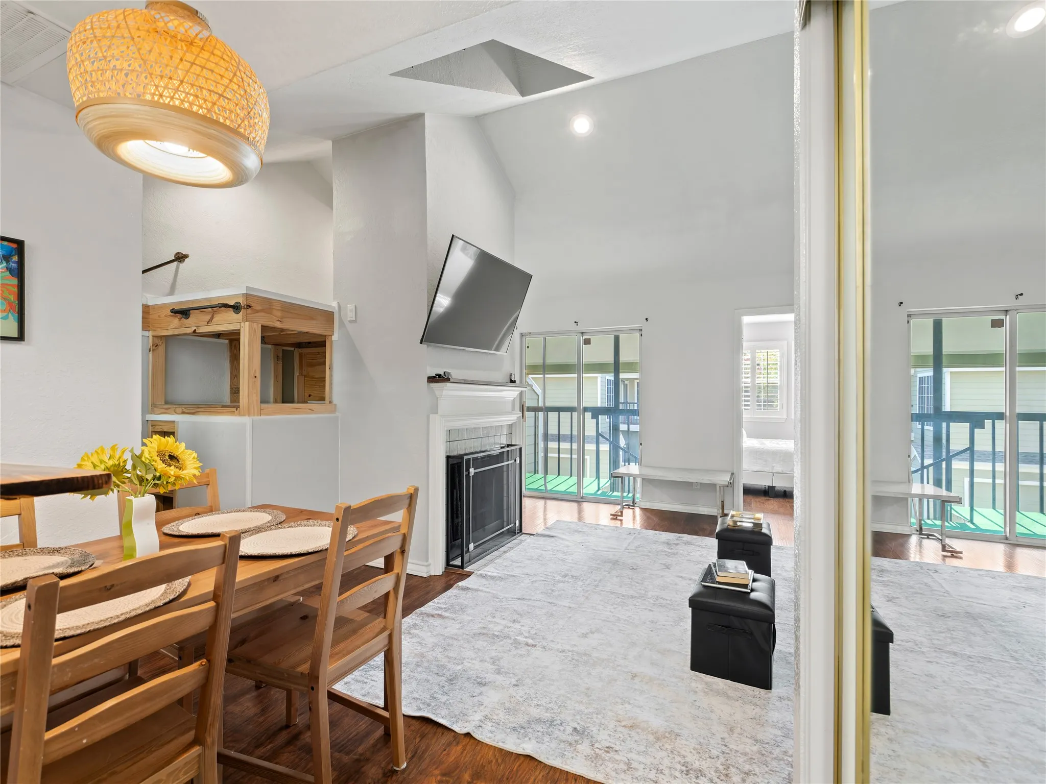 Vaulted ceiling, wood-finish flooring, built-in fireplace, sliding glass doors, and a decorative light fixture
