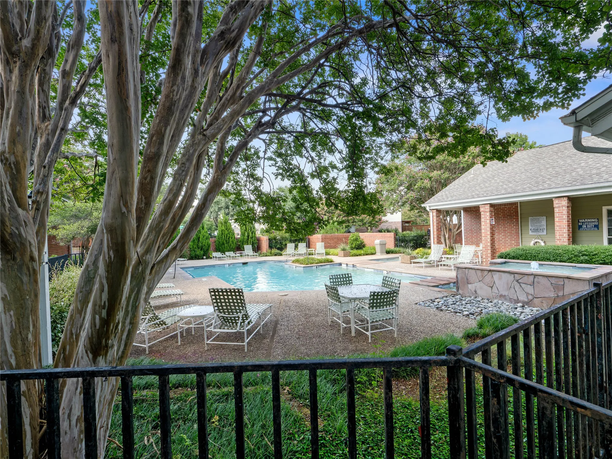 Outdoor pool area with surrounding hardscaping, a water feature, and mature trees