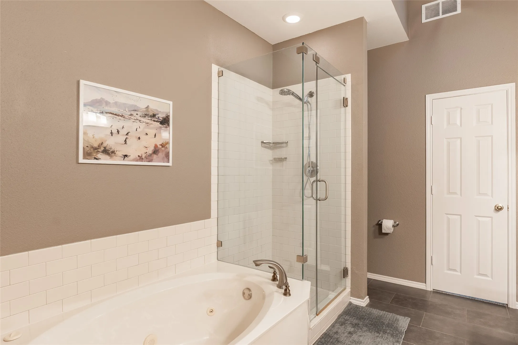Jetted soaking tub, glass-enclosed shower, white subway tile surround, tile flooring, and recessed lighting