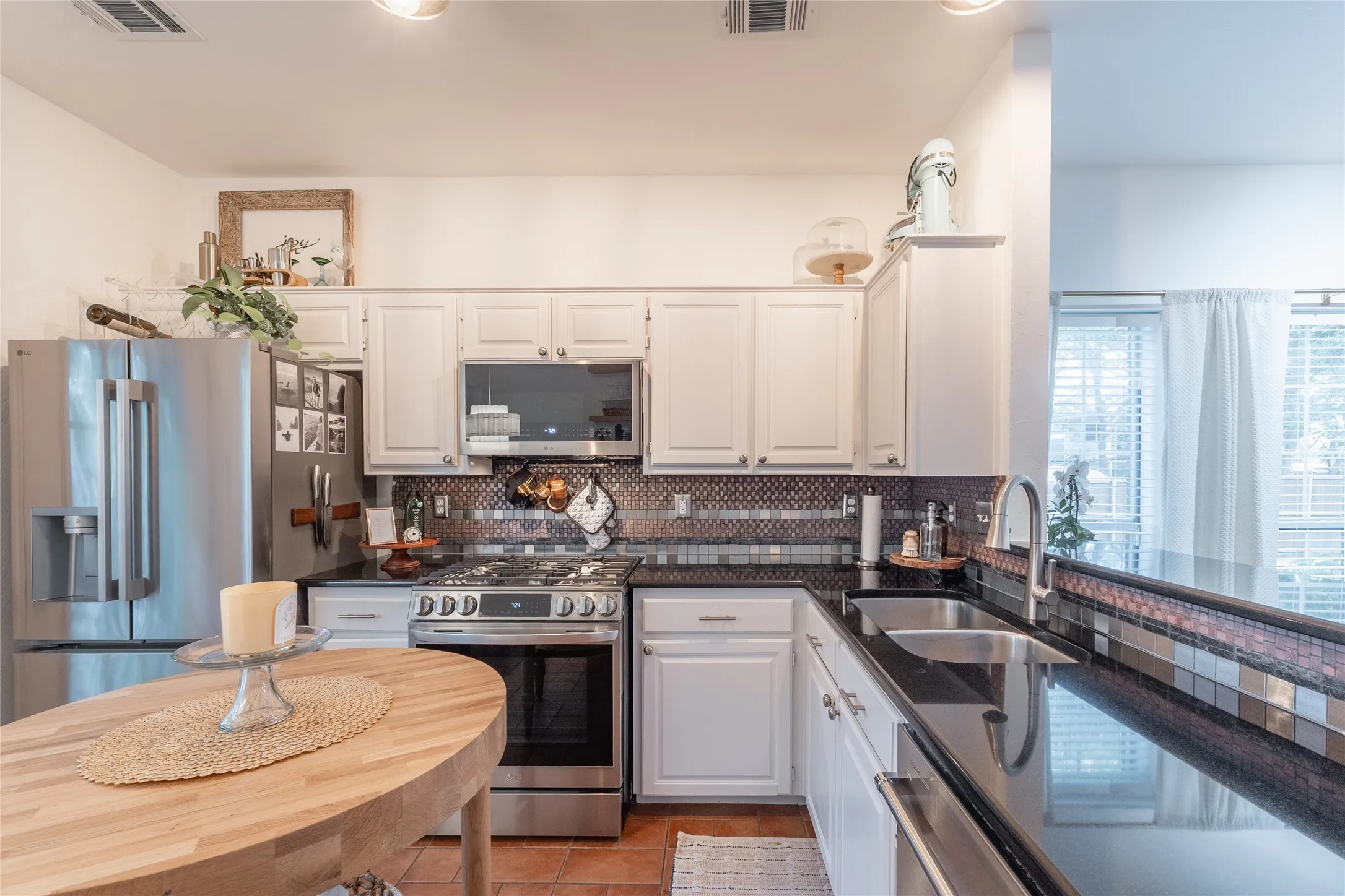 White cabinetry with brushed nickel pulls, black stone countertops, mosaic tile backsplash, and stainless steel appliances
