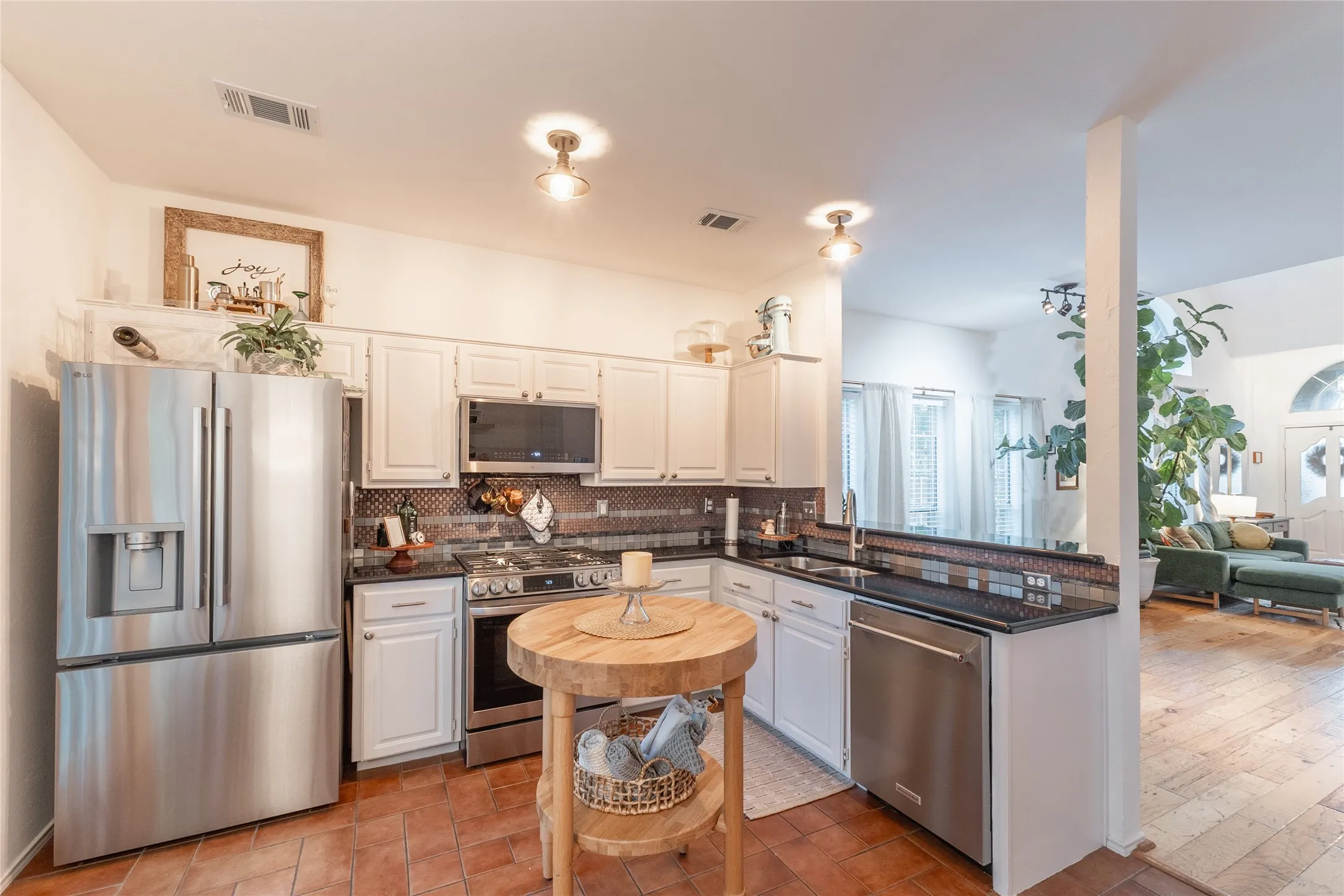 Stainless steel appliances, white cabinetry, dark stone countertops, and a tiled backsplash