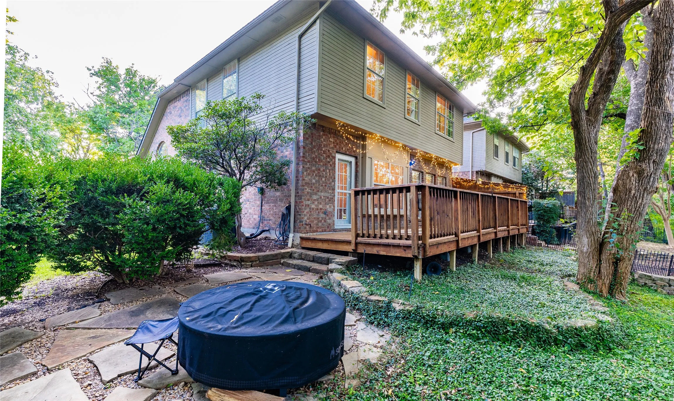 Expansive rear wood deck with railing, stone retaining walls, mature trees, and a stone paver patio