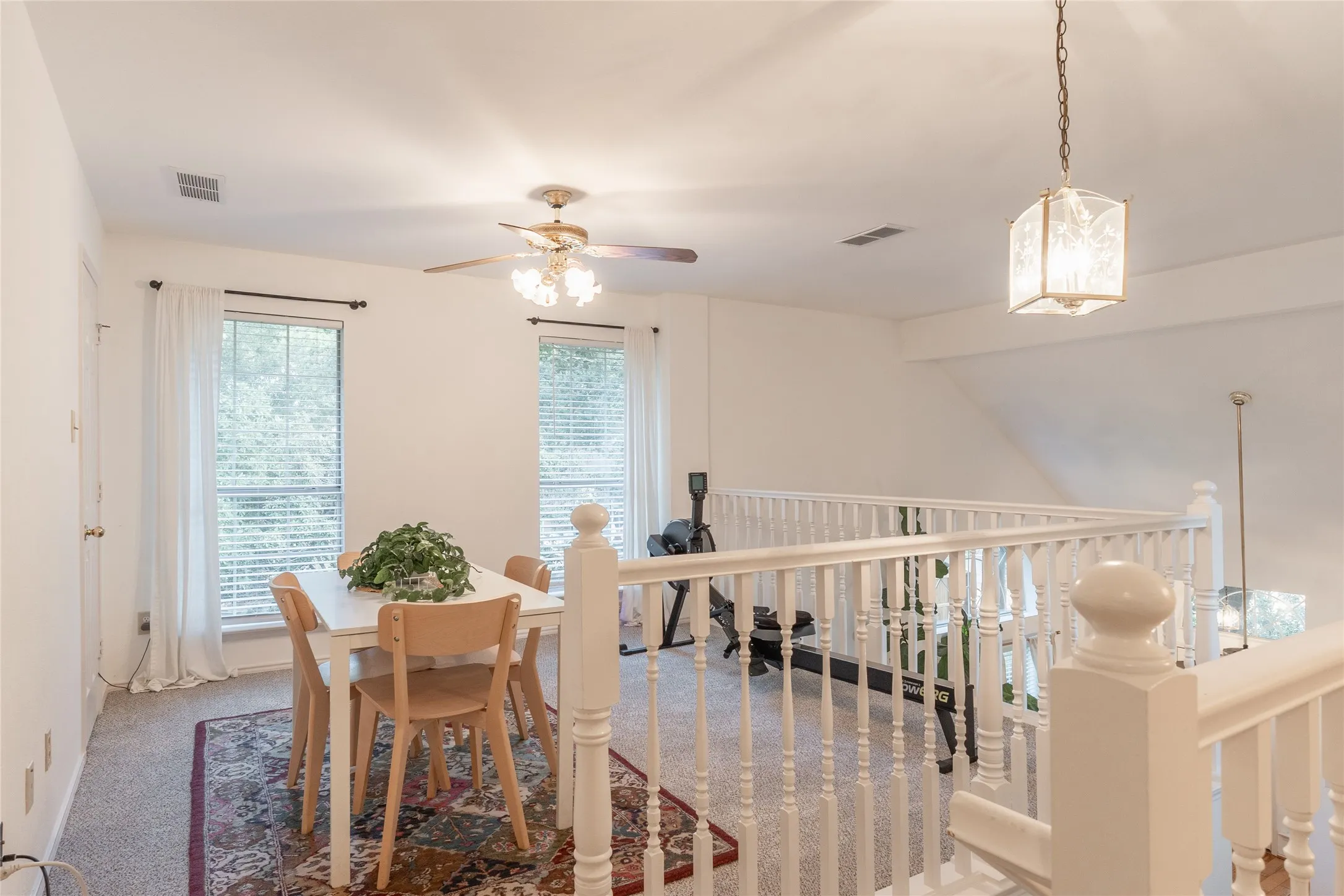 Loft space featuring a white spindle railing, carpet flooring, and a ceiling fan with light fixture