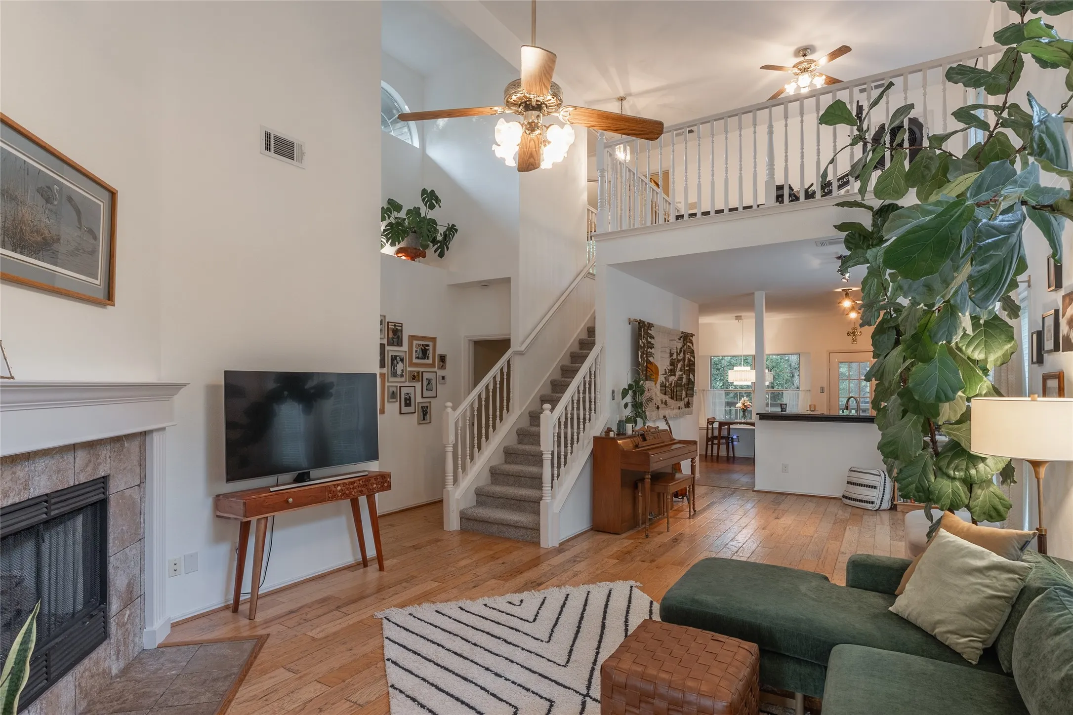 Hardwood flooring, fireplace with tile surround, vaulted ceiling with ceiling fan, white staircase with carpeted treads, and an open loft area with white railing