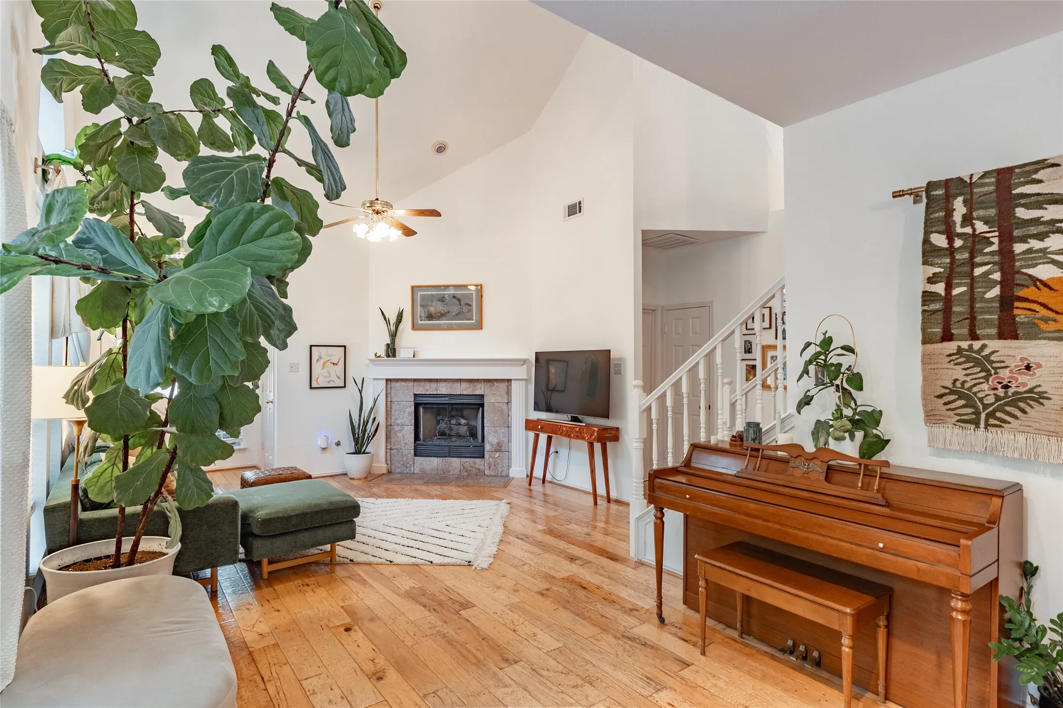 Vaulted ceiling, ceiling fan, wood-finish flooring, fireplace with stone surround, and white painted balusters