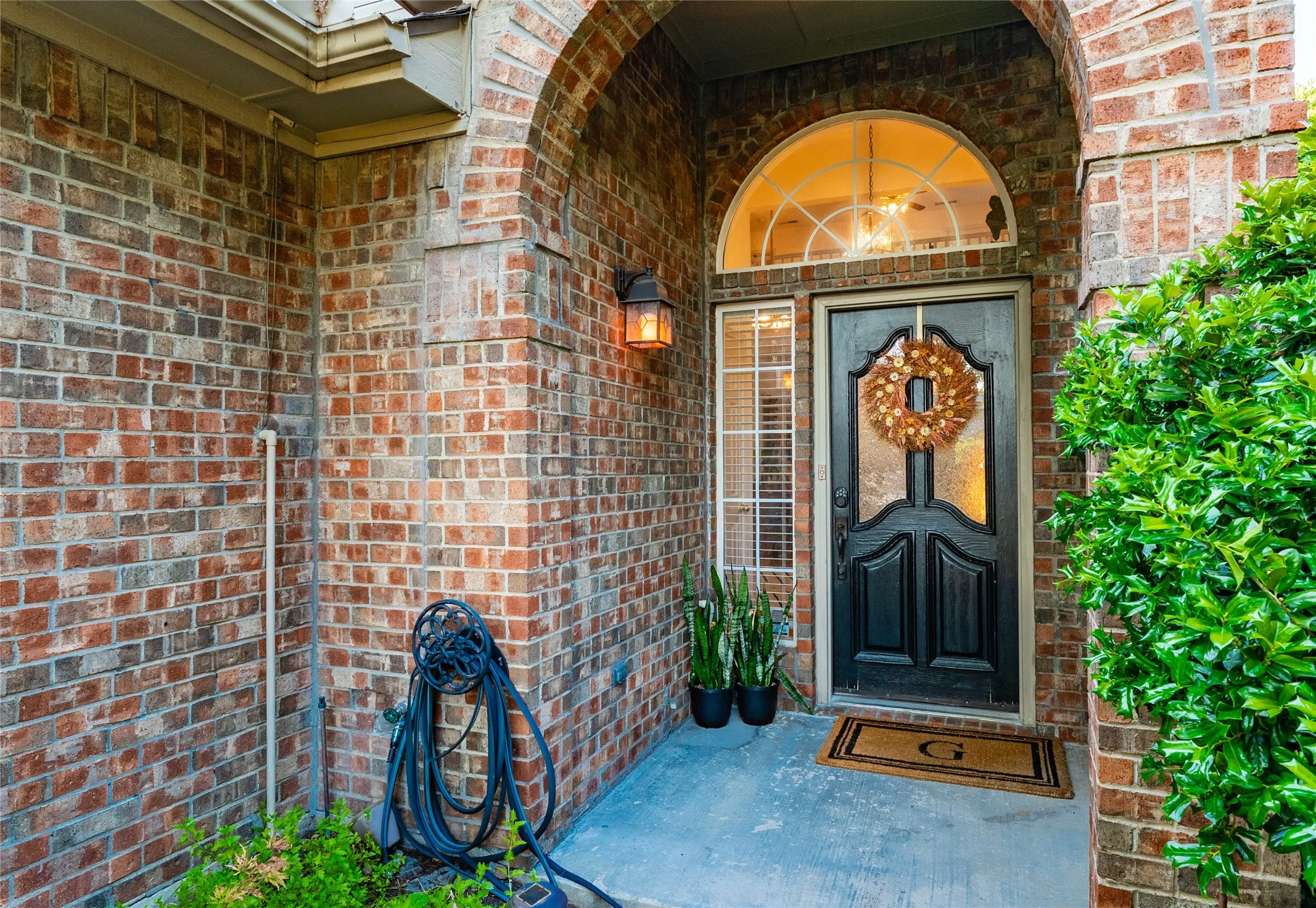 Brick facade with an arched entry, a dark paneled door featuring decorative glass, and a transom window above