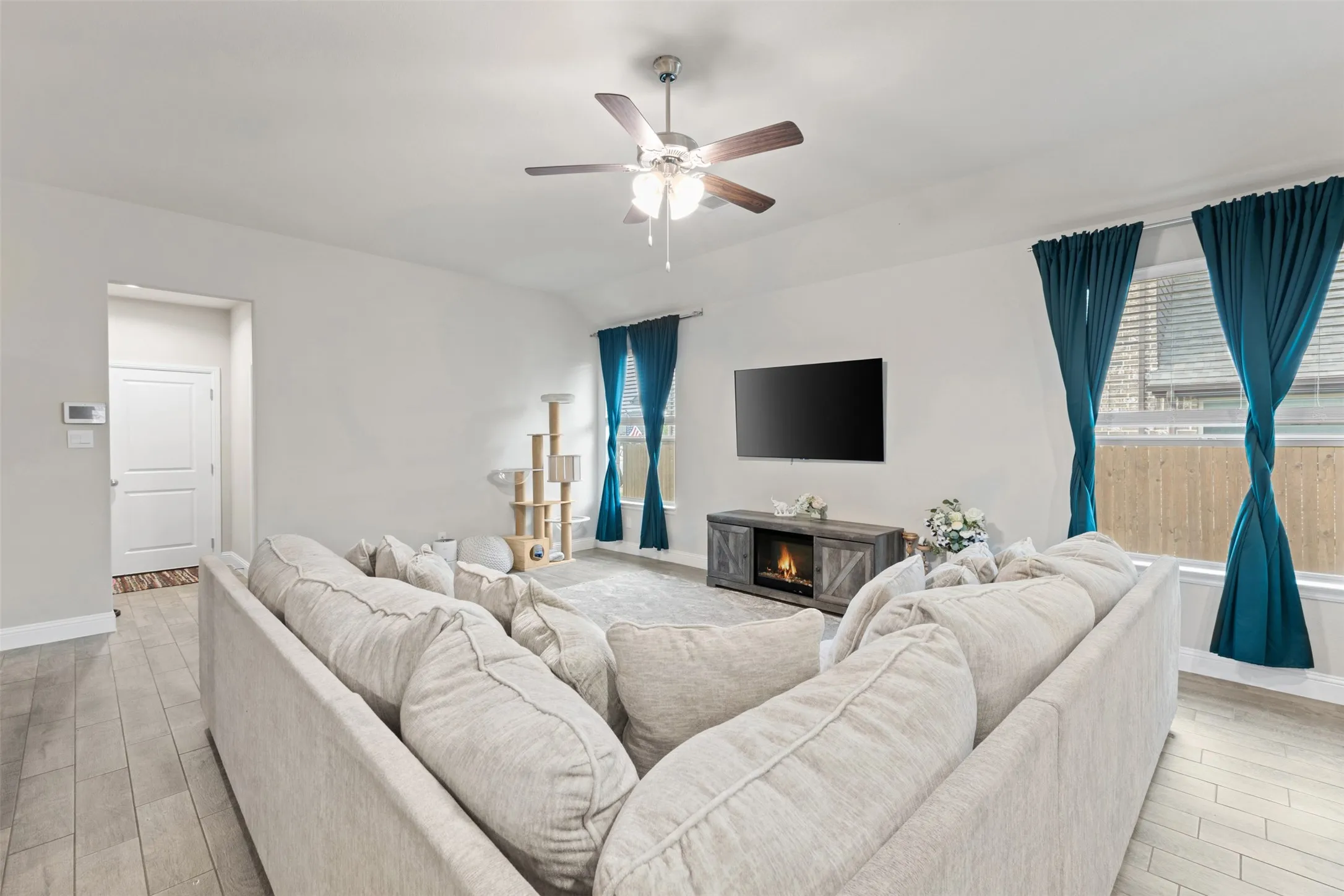 Vaulted living area featuring wood-finish flooring, a ceiling fan, and large windows
