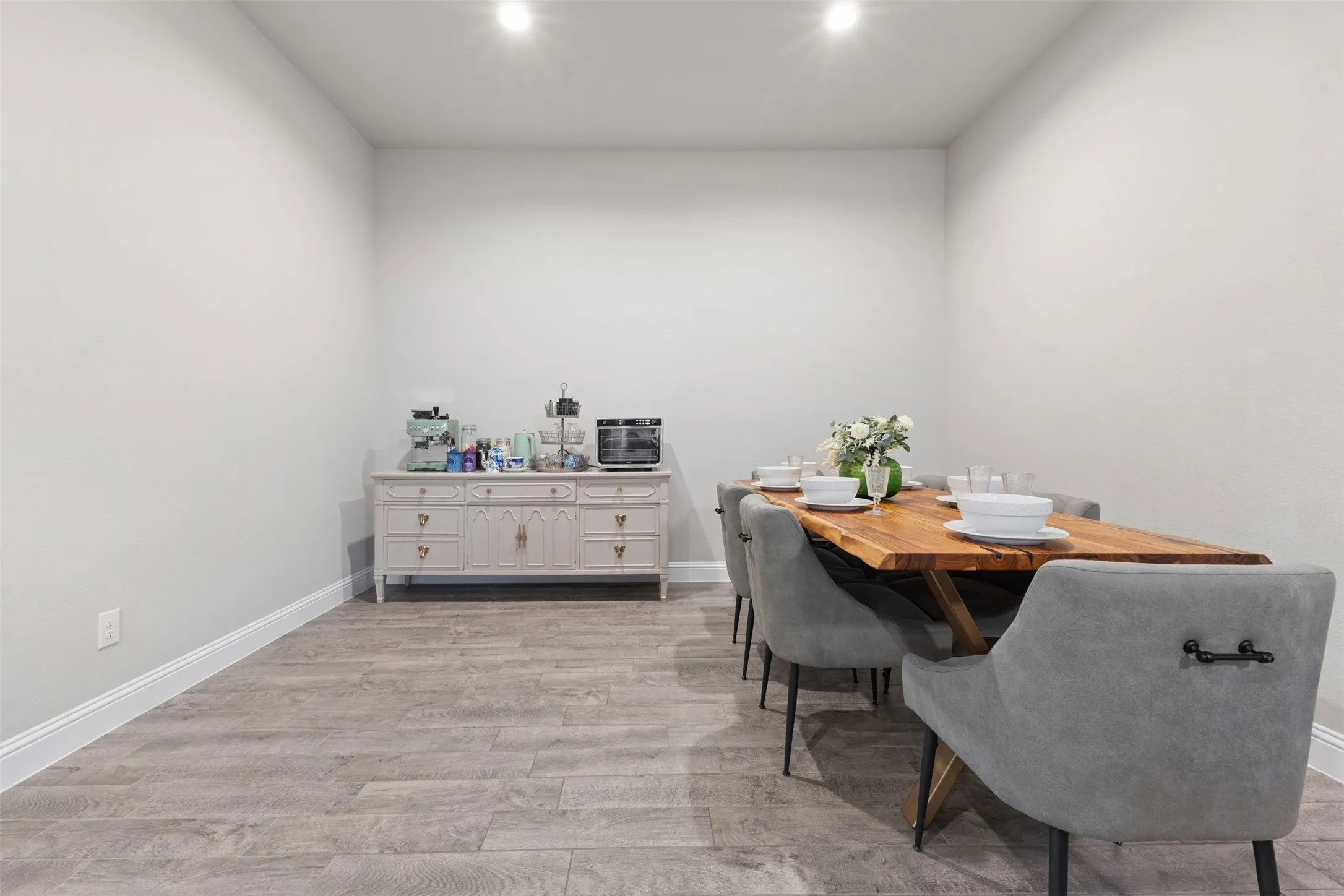 Recessed ceiling lighting, light gray wall paint, wood-finish flooring, white baseboards