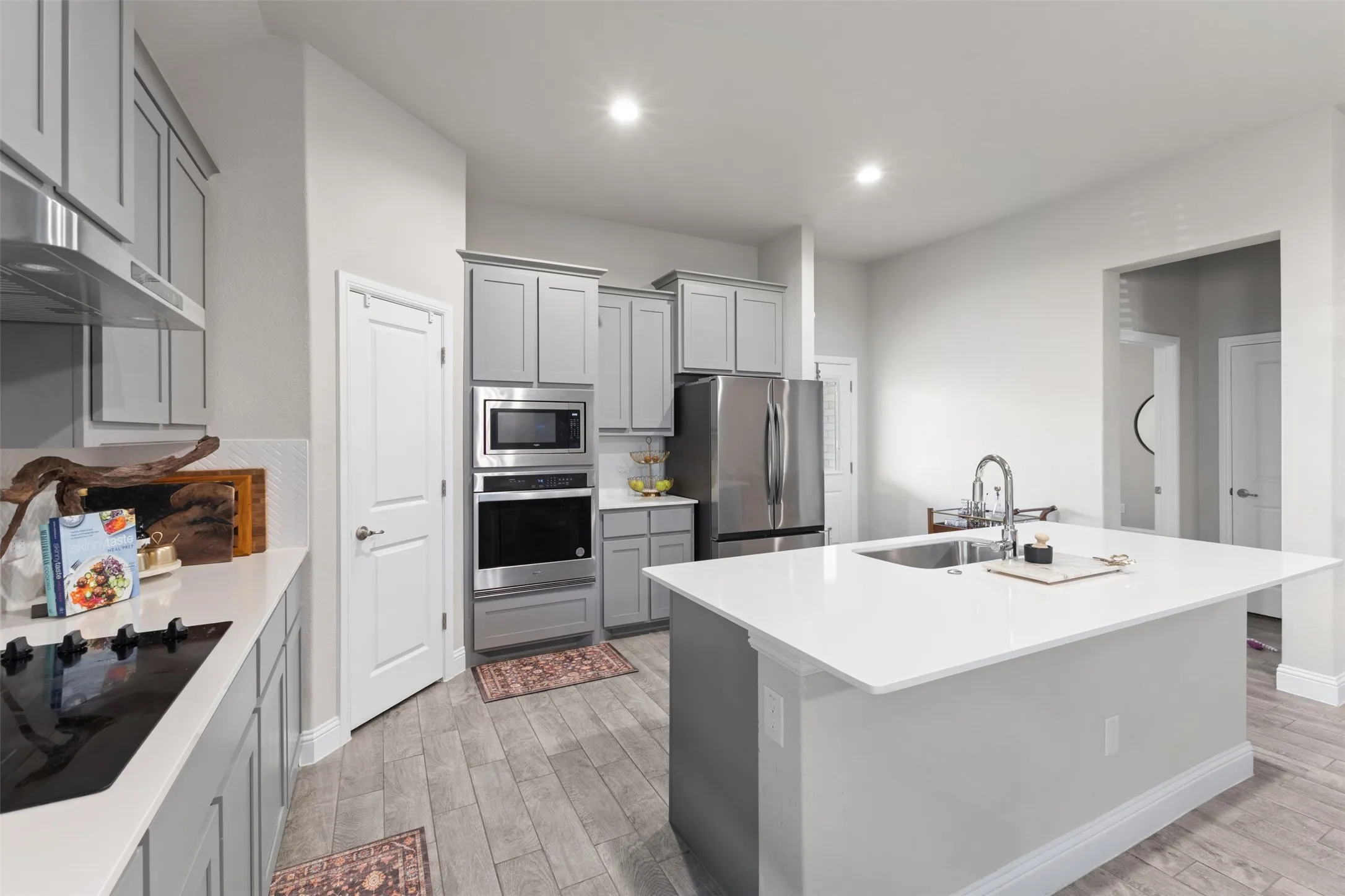 Spacious kitchen featuring an island with a sink, stainless steel appliances, grey cabinetry, light countertops, and wood-finish flooring