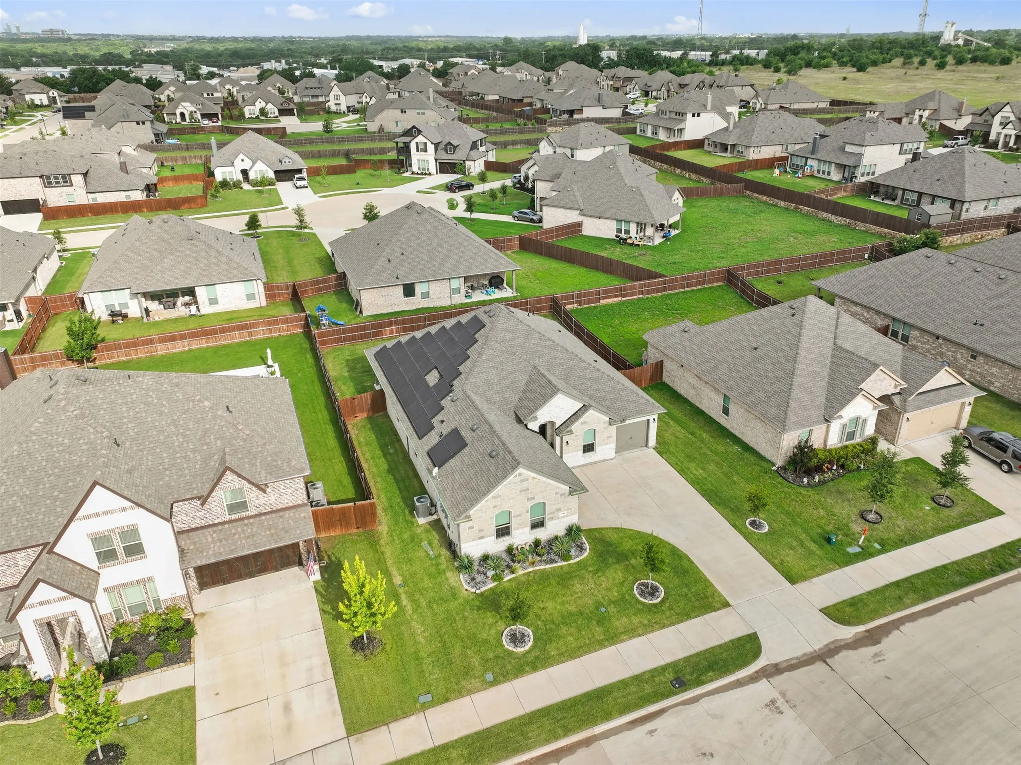 New construction residential development featuring mature trees, manicured lawns, and solar panels