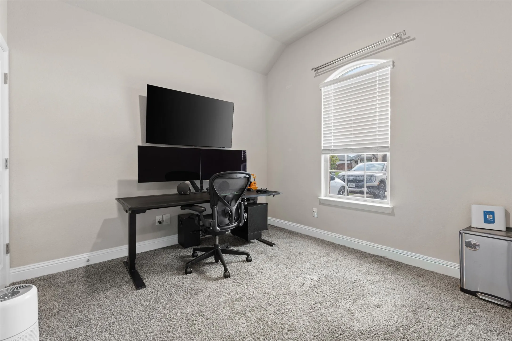 Vaulted ceiling, arched window, soft gray wall paint, white trim, and gray carpeted flooring