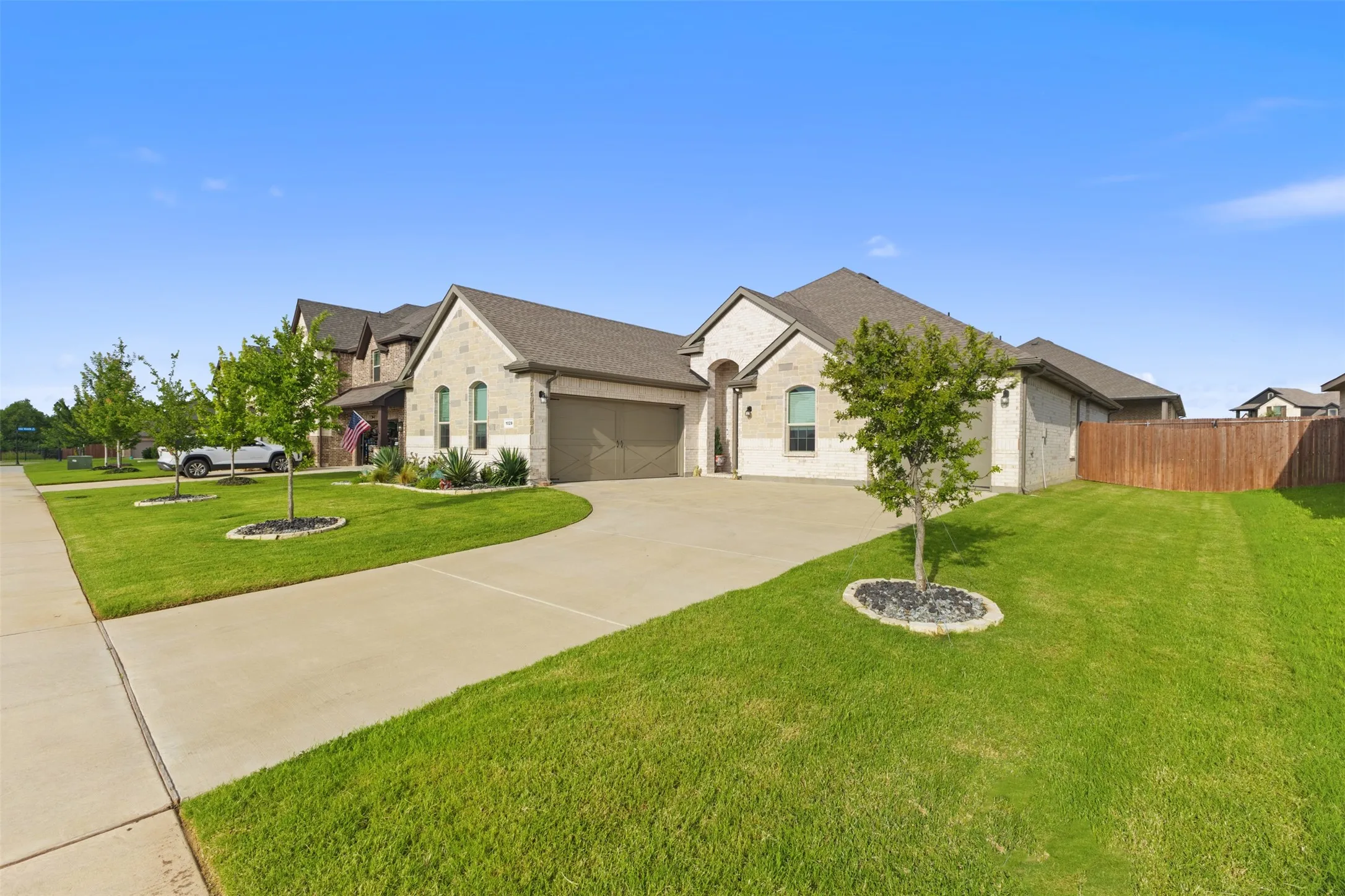Stone and brick exterior with an attached garage, concrete driveway, and a wood privacy fence