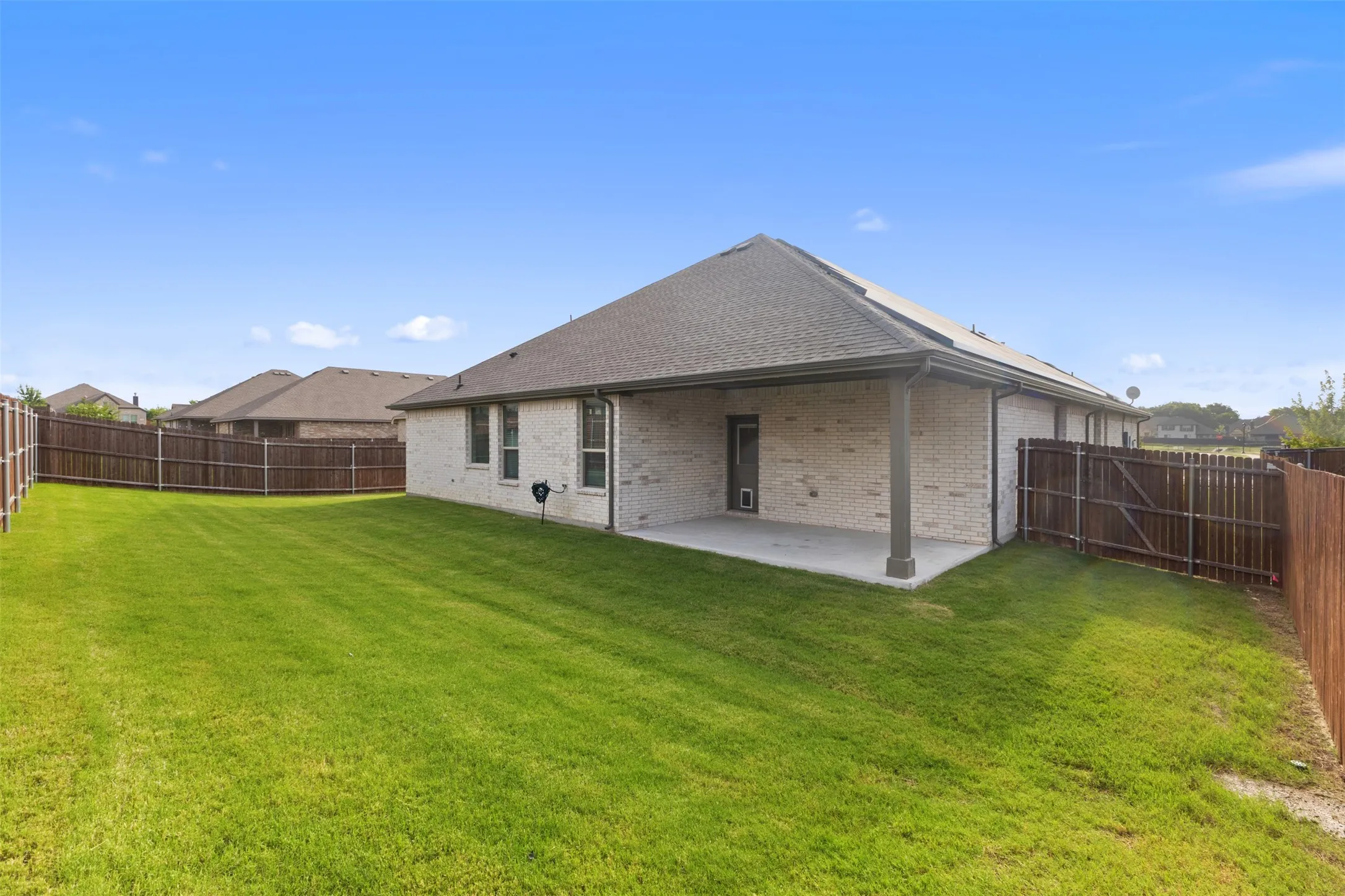 Expansive backyard featuring a manicured lawn, full privacy fencing, and a covered concrete patio