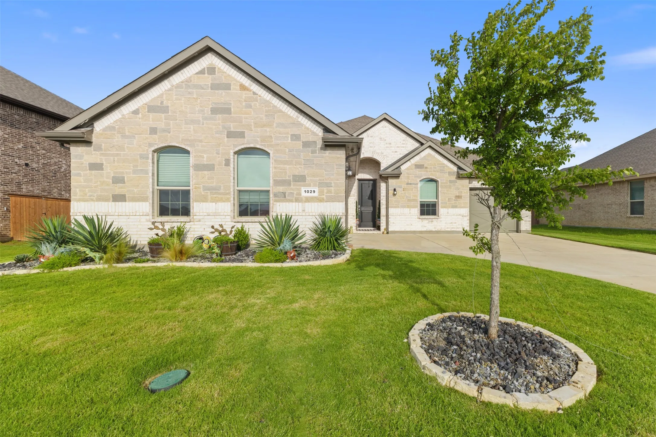 Light-colored brick and stone exterior with a gabled roofline, arched windows, and a concrete driveway