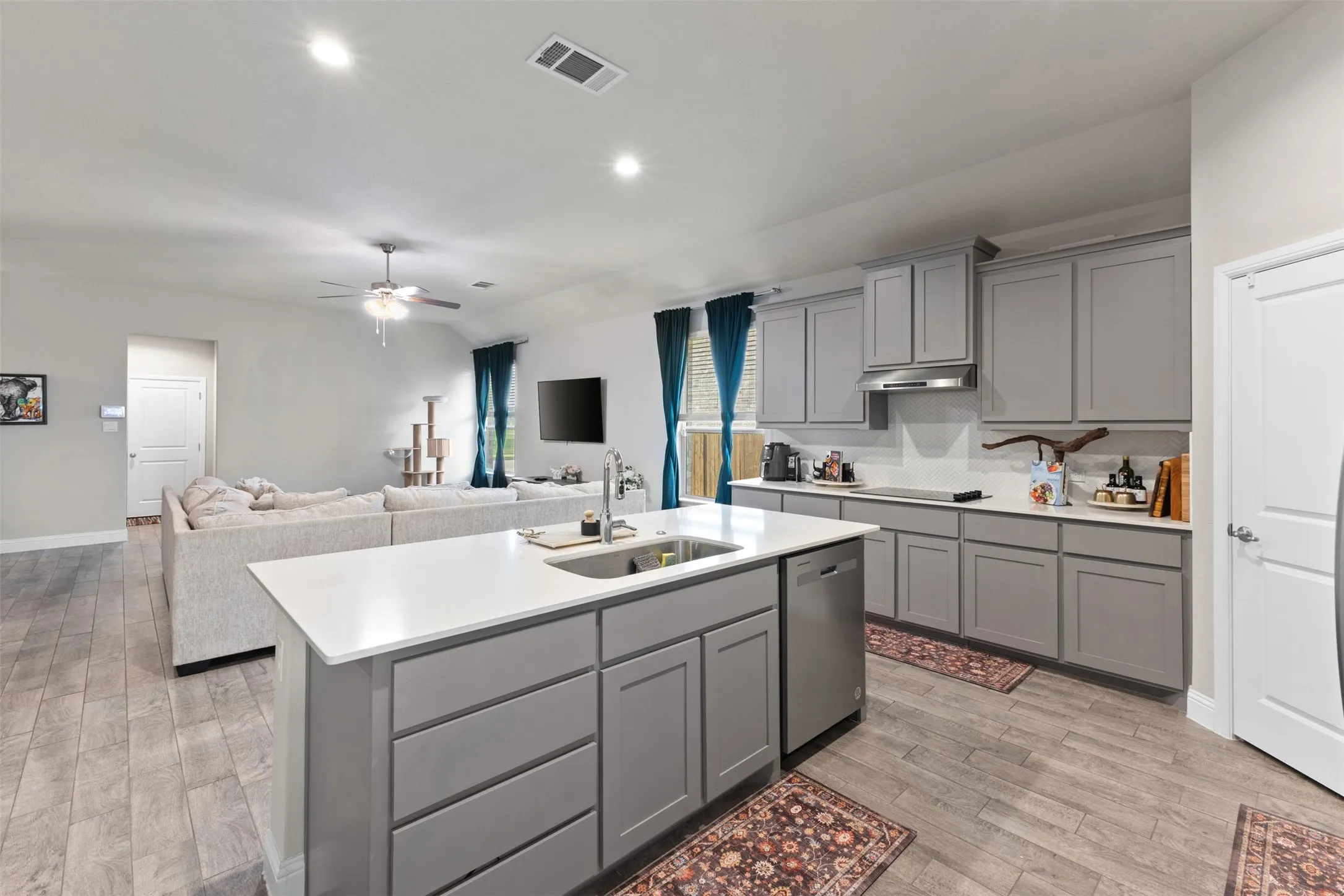 Open-concept living space featuring a kitchen island with sink, gray cabinetry, stainless steel appliances, and wood-finish flooring