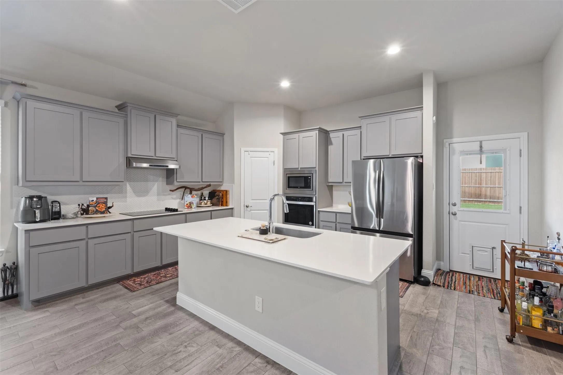 Kitchen featuring gray cabinetry, stainless steel appliances, a white island with an undermount sink, and wood-finish flooring