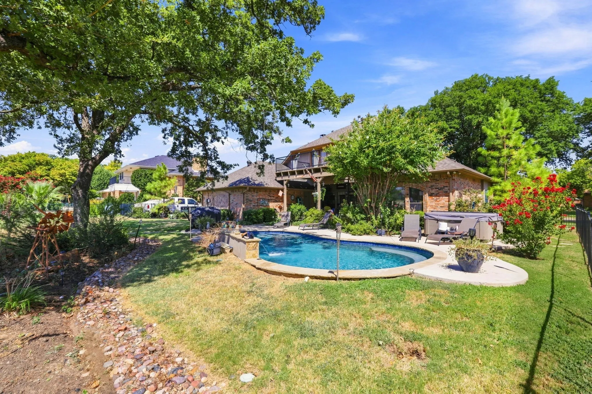 Backyard featuring an in-ground swimming pool, hot tub, brick exterior, and mature landscaping