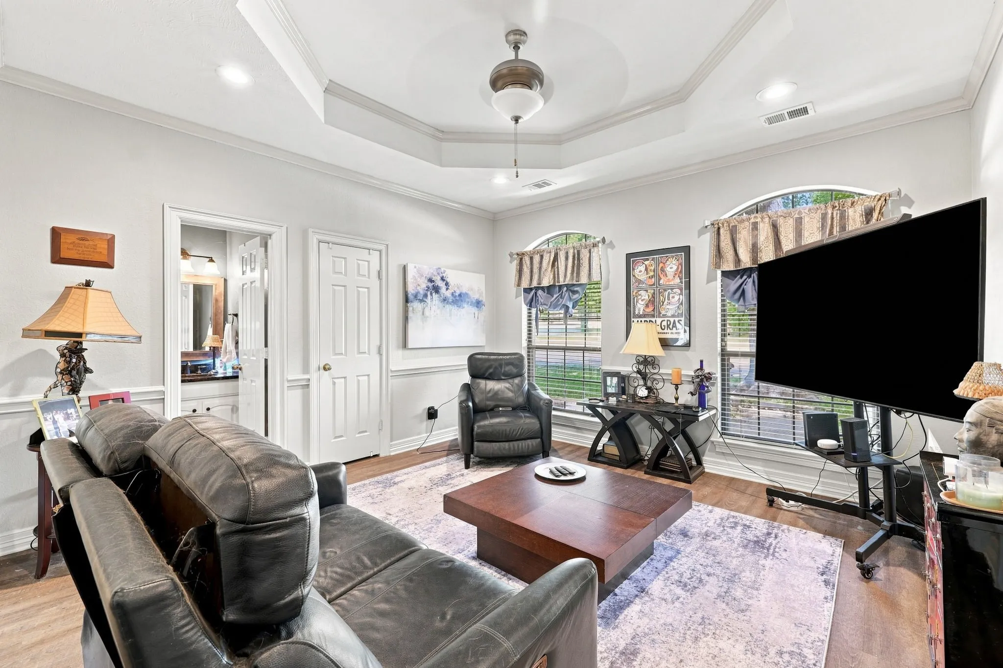 Tray ceiling with crown molding, recessed lighting, wood-finish flooring, and arched windows