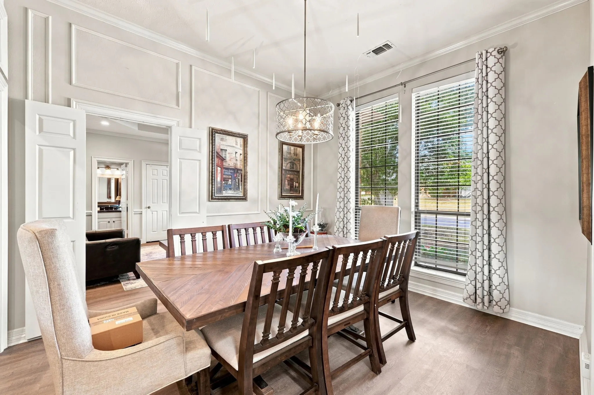 Wood-finish flooring, decorative wall molding, and dual windows with blinds and patterned curtains