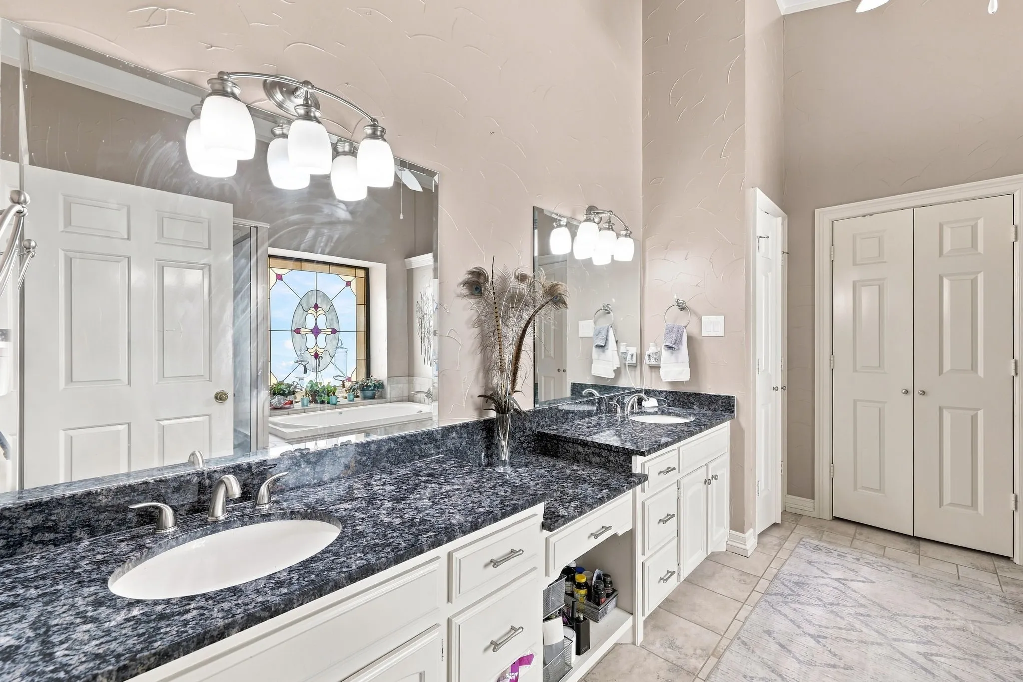 Dual vanities with dark granite countertops, individual undermount sinks, white cabinetry, and brushed nickel hardware