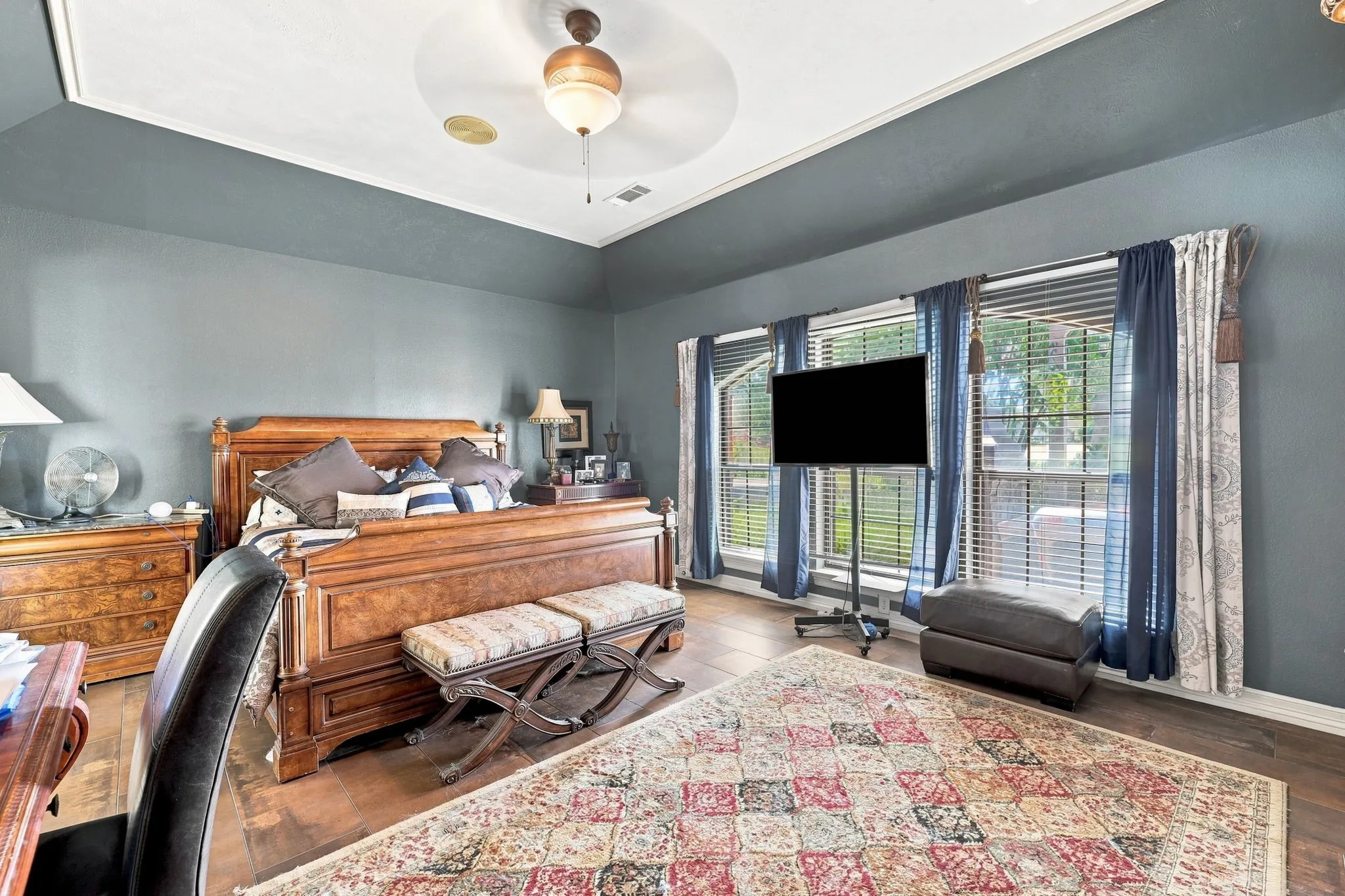 Tray ceiling with a decorative ceiling fan, wood-finish flooring, and multiple windows with blinds and drapery