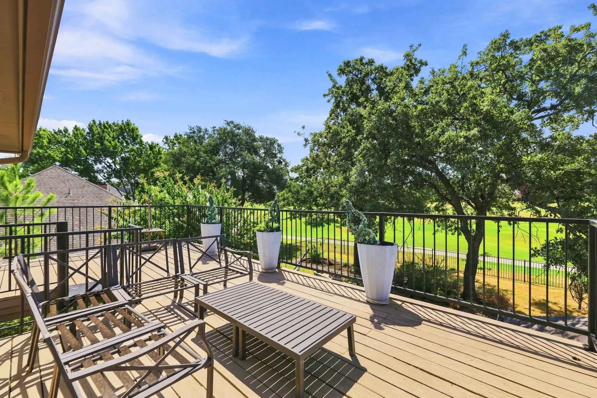 Expansive wood-finish deck with black metal railing, offering abundant natural light and green landscape