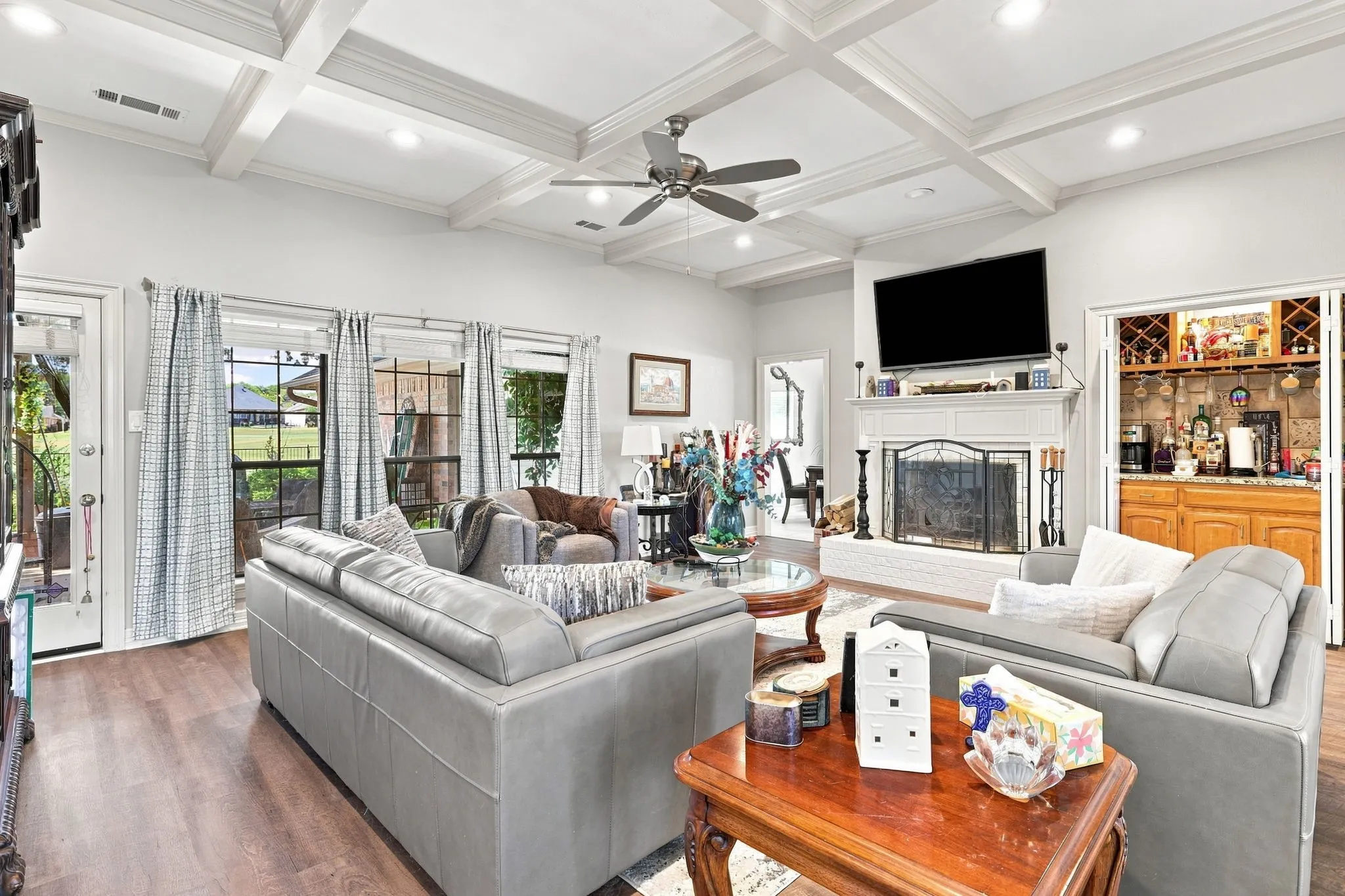 Coffered ceiling, recessed lighting, ceiling fan, wood-finish flooring, and a built-in wet bar with cabinetry