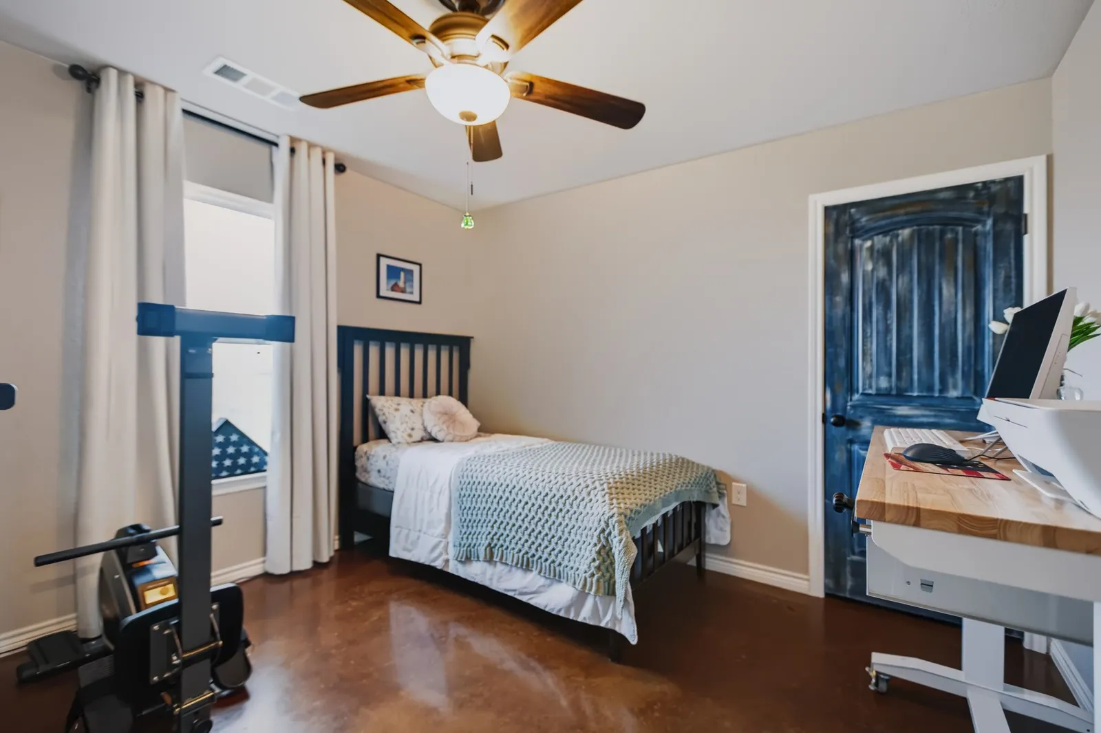 Guest Room 1
Wood-finish flooring, ceiling fan with light fixture, window with roller shade and curtains, and a distressed blue paneled door