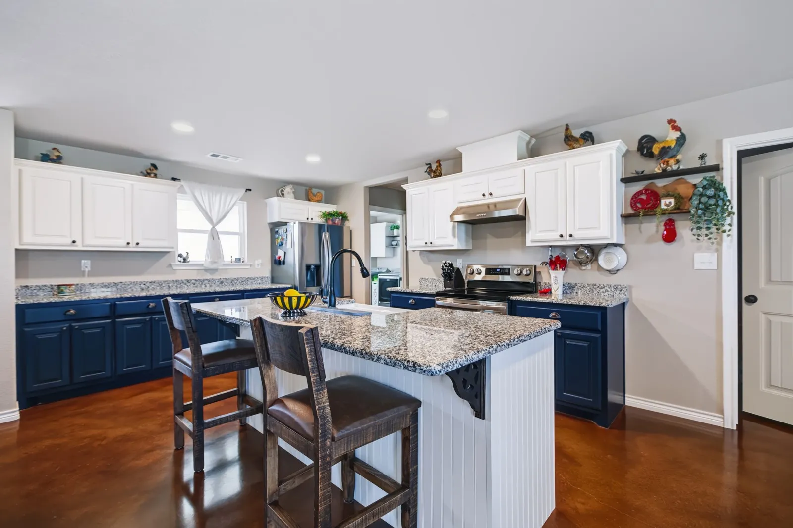 Kitchen featuring two-tone cabinetry with white upper and navy lower cabinets, a central island with a granite-style countertop, stainless steel appliances, and a built-in oven and range