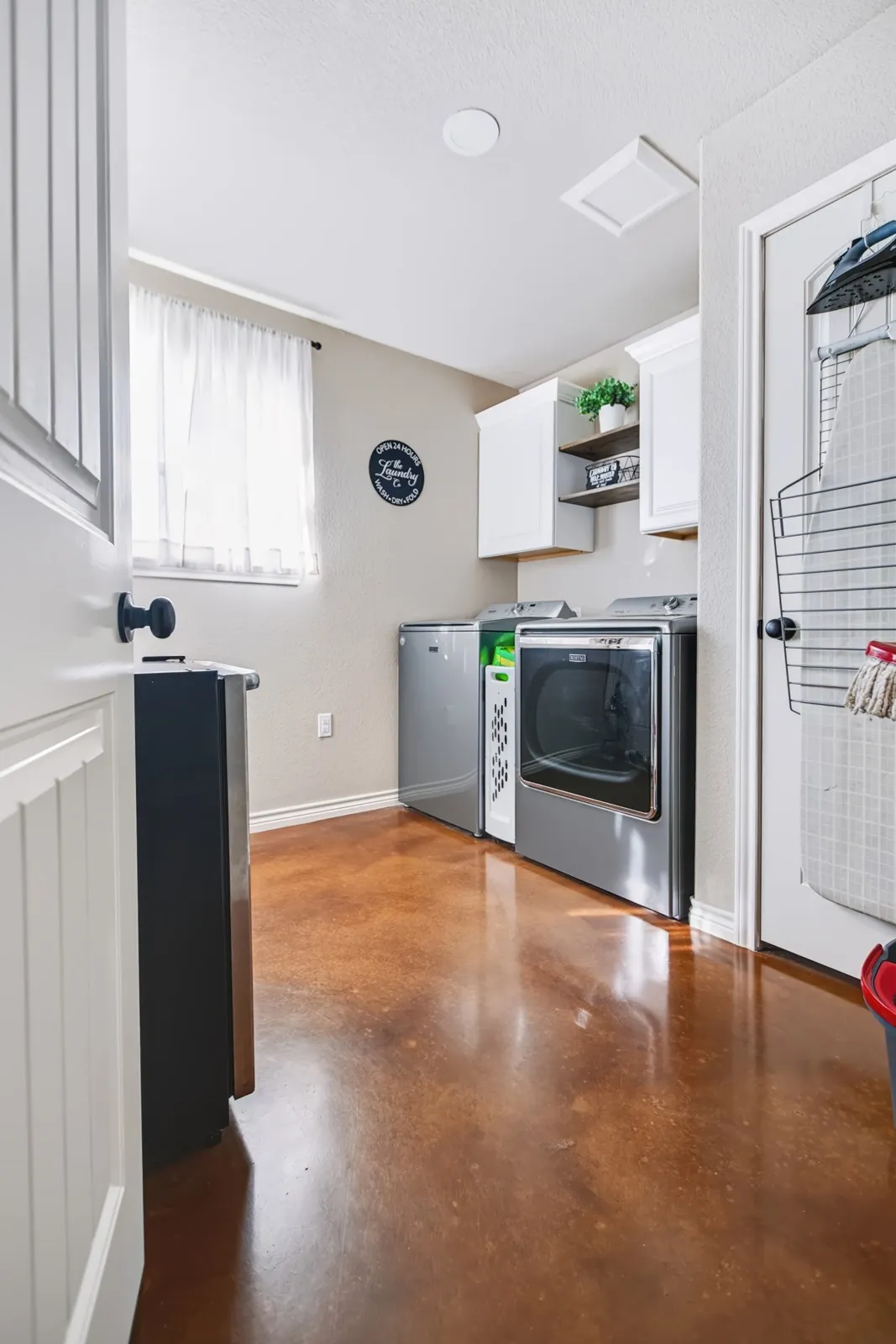 Laundry room featuring stained concrete flooring, white cabinetry, and a window for natural light
