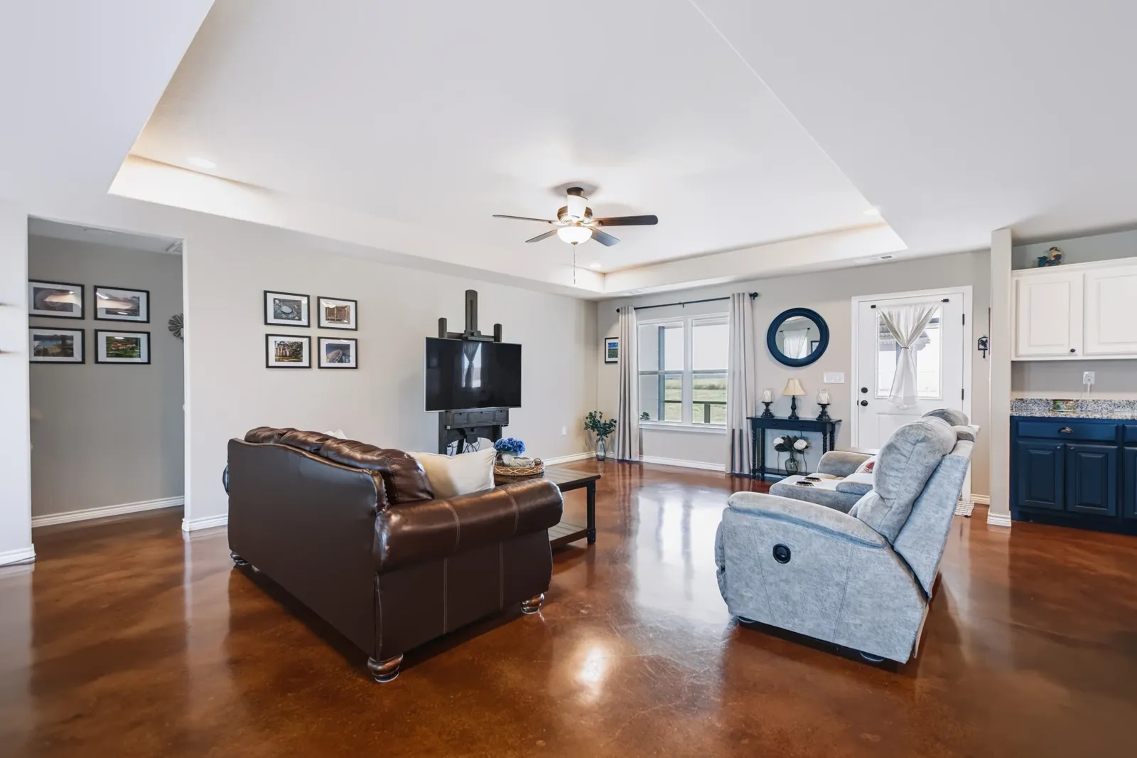 Expansive living area with high tray ceiling, wood-finish flooring, and recessed lighting