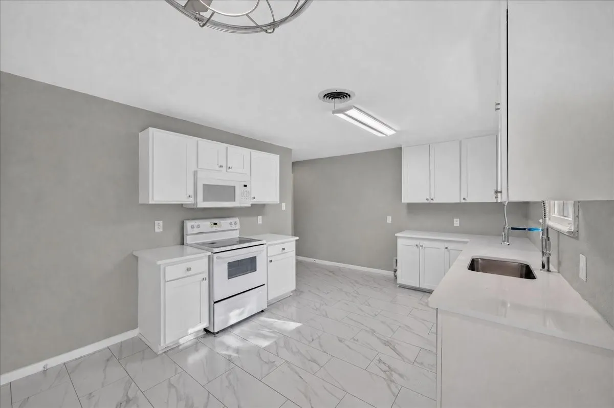 Kitchen featuring white cabinetry, white appliances, light-toned countertops, and light-colored tile flooring