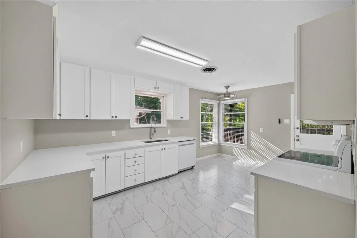White shaker cabinetry, light-toned countertops, tile flooring, built-in dishwasher, and a bay window