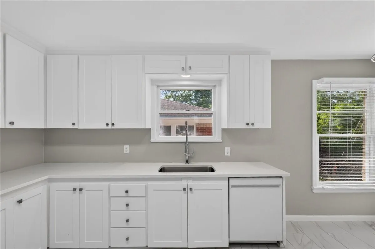 White cabinetry with dark hardware, undermount stainless steel sink, light-toned countertops, and integrated dishwasher