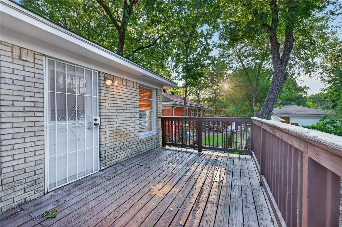 Spacious wood deck with a privacy railing, brick exterior, exterior lighting fixture, and a security screen door