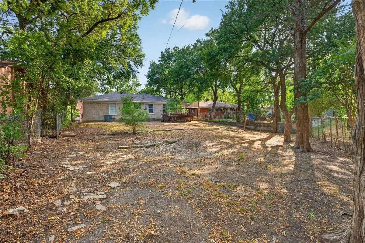 Expansive rear yard with mature trees and a chain-link fence